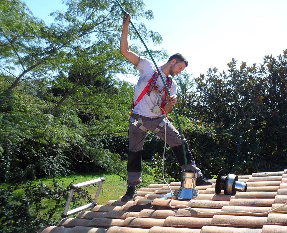 Ramonage d’un conduit de poêle à bois par un professionnel sur une toiture